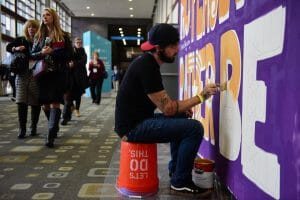 Man Painting a wall while sitting on a bucket