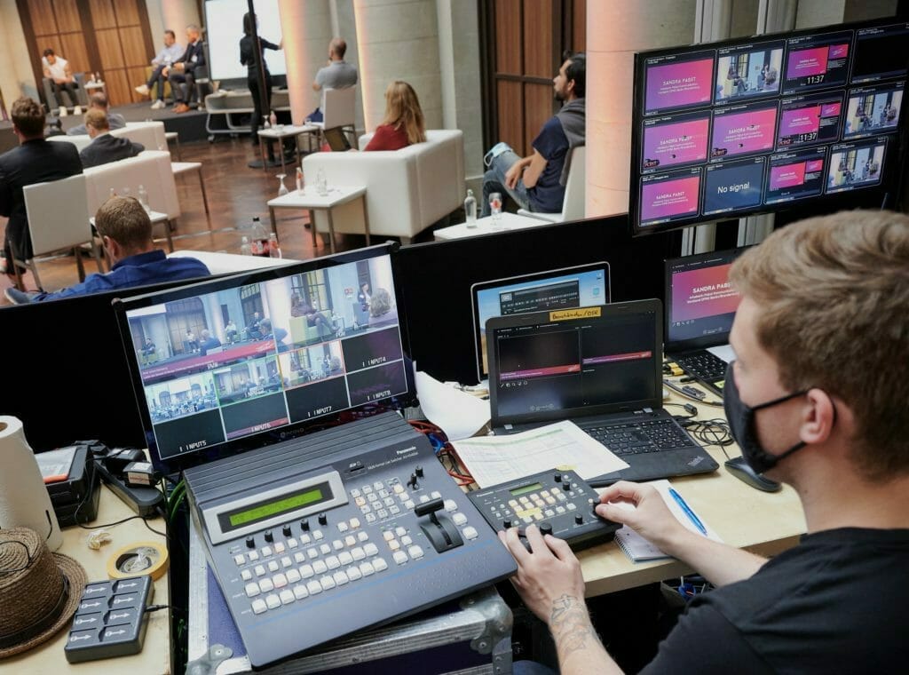 An AV technician sits behind a set up of several laptops, screens and controllers