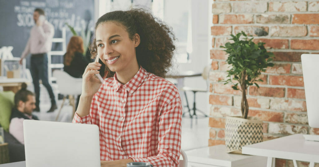 Eine Community-Managerin sitzt im Büro an ihrem Laptop und telefoniert.