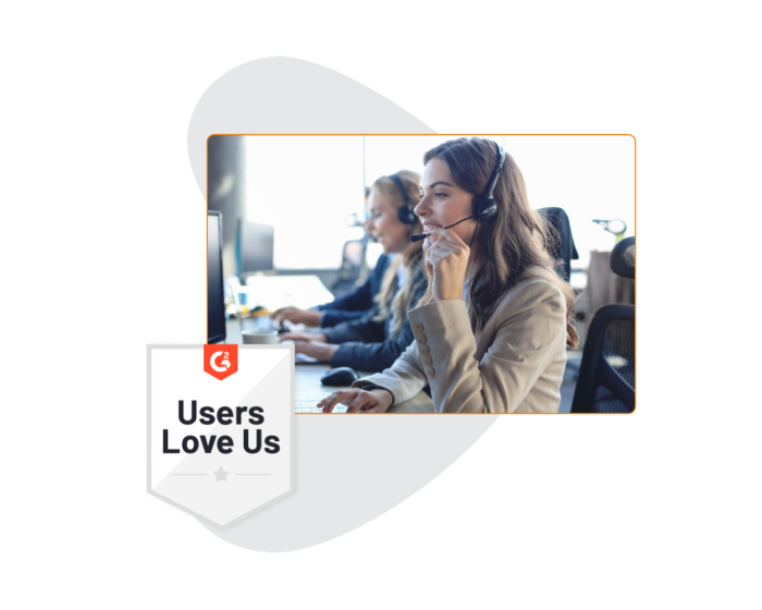 A woman in a call centre environment with a headset in front of a computer, with a G2 "Users Love Us" badge to one side