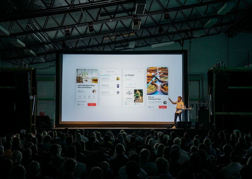 An Audience at an event looking at a large screen on stage.