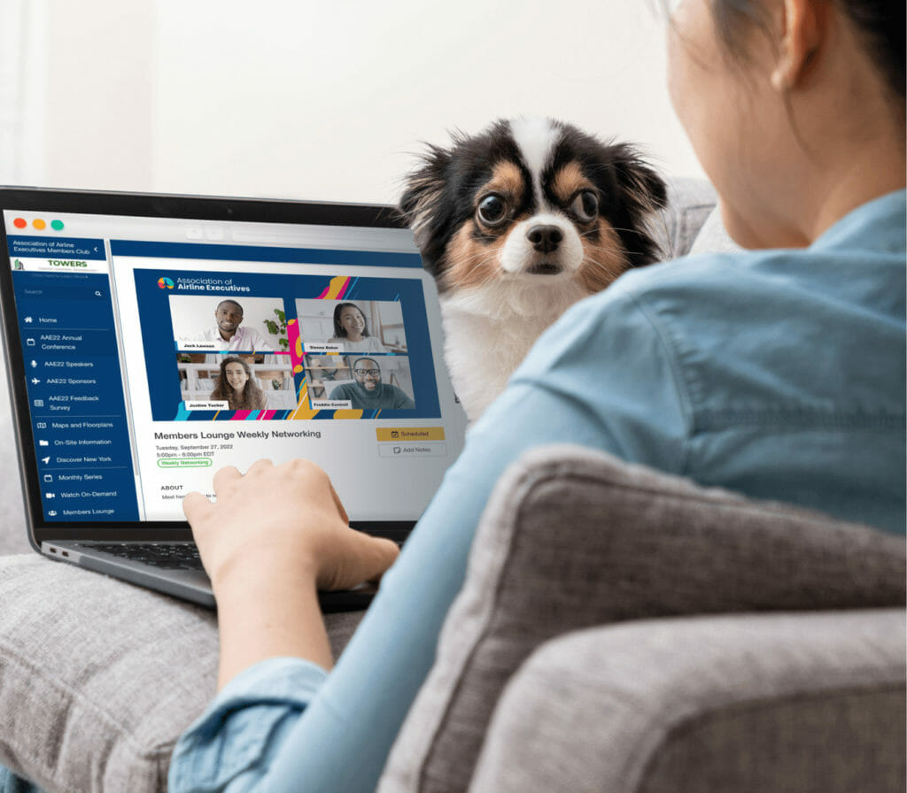 A woman watching a virtual event on her laptop while a dog sits on her lap.