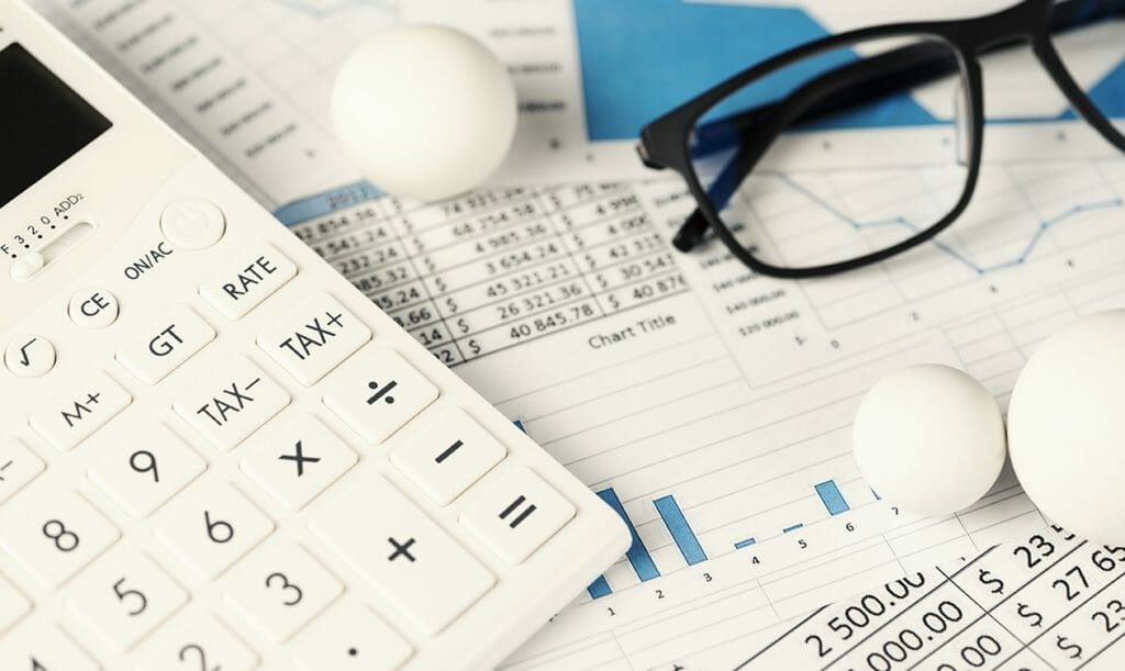 A calculator, a pair of glasses, and some white balls over printed charts
