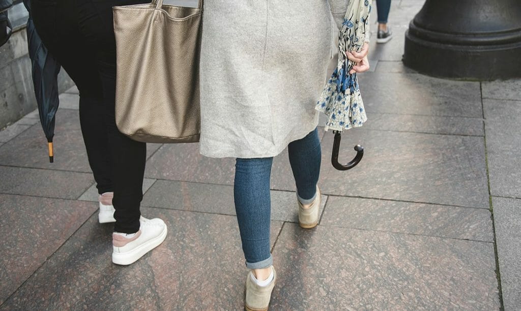 Two women holding umbrellas and walking along a sidewalk.