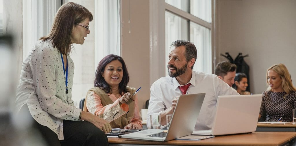 Drei Kolleg*innen sitzen um einen Laptop und diskutieren die Eventstrategie.