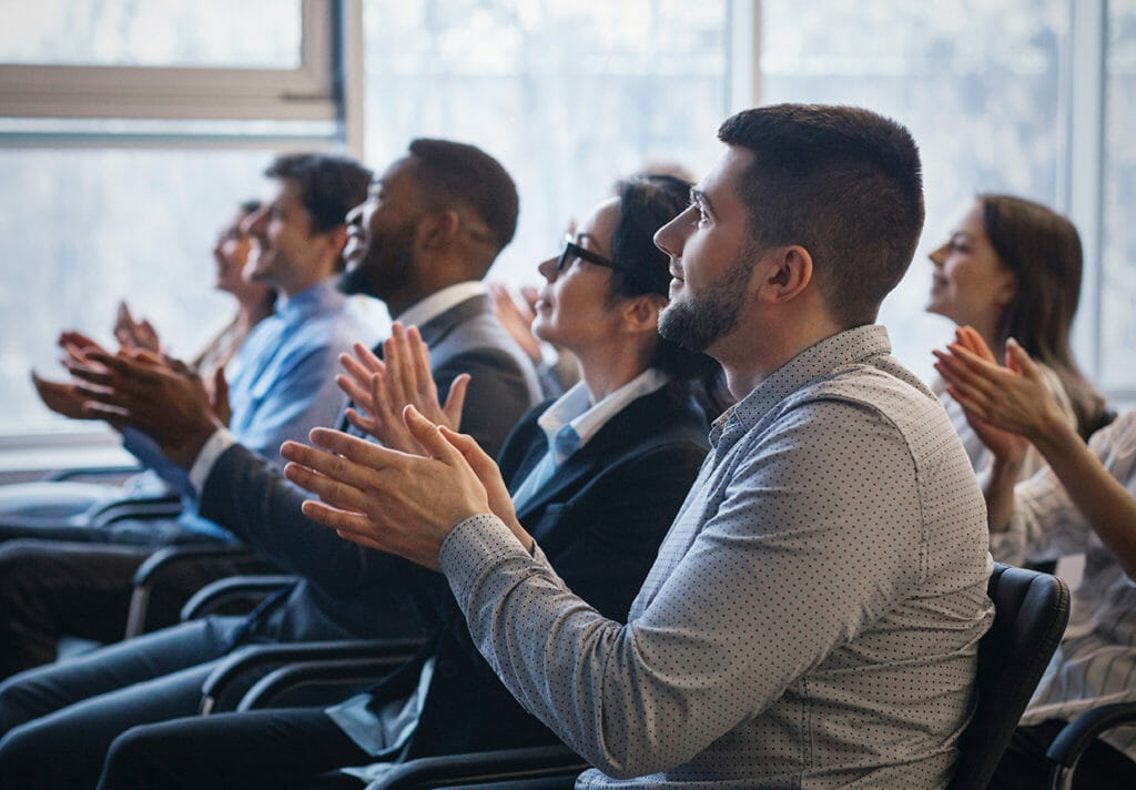 In-person event attendees listening to a speaker and clapping 