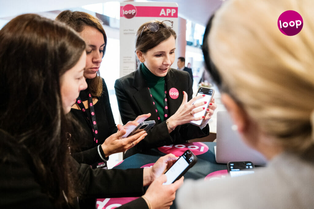 Besucherinnen einer Veranstaltung lassen sich die Event-App von EventMobi erklären.