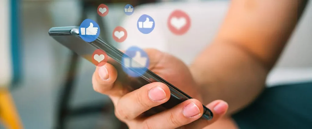 Smartphone in einer Hand, überlagernd eingeblendet Social-Media-Symbole.