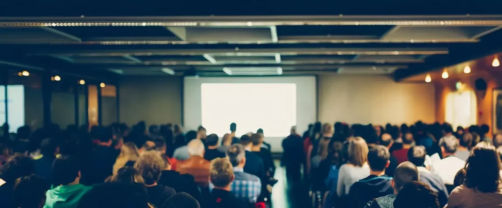 Vor-Ort-Event, bei dem das Publikum in einem Konferenzsaal vor einer Großbildleinwand sitzt.