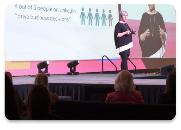 A speaker presenting on stage to a seated audience.