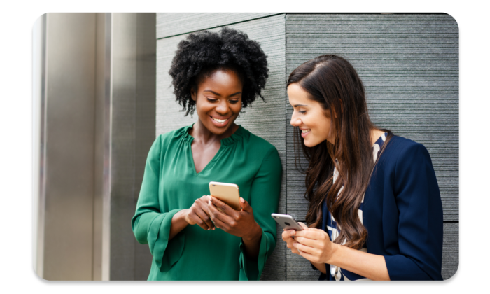 Two women smiling while one shows the other something on her phone.