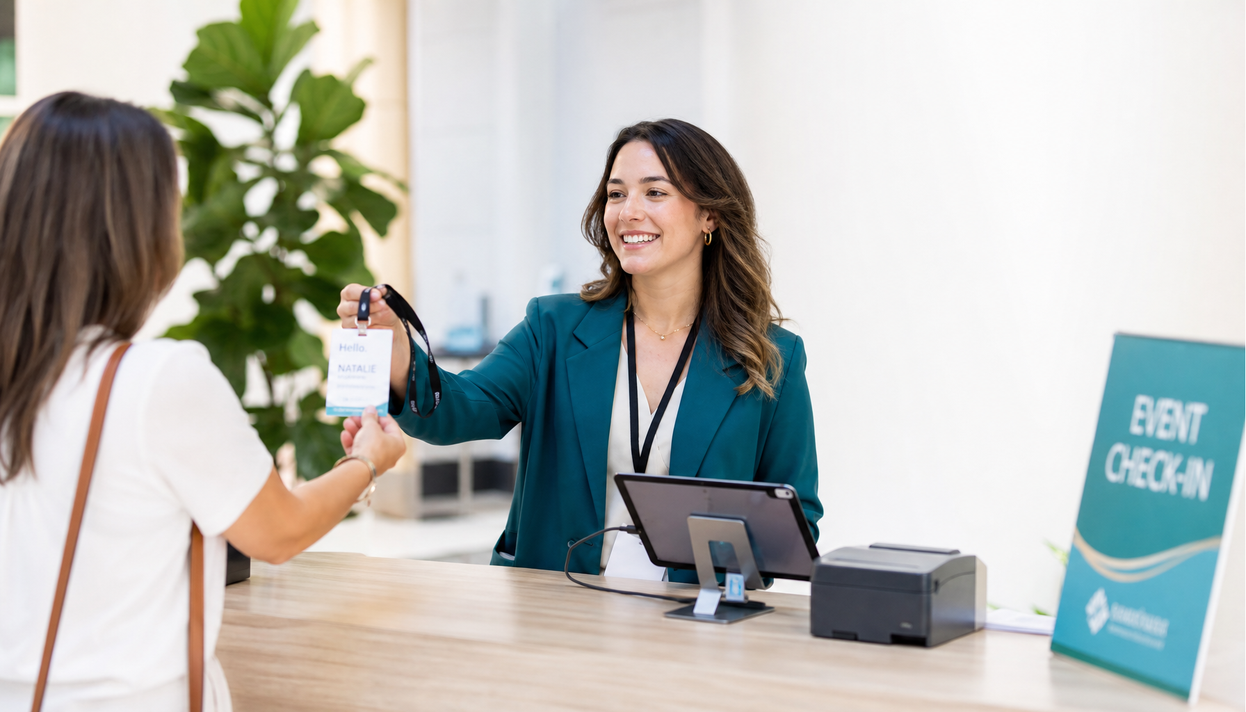 Event staff member handing a freshly printed badge to an attendee at a modern check-in desk