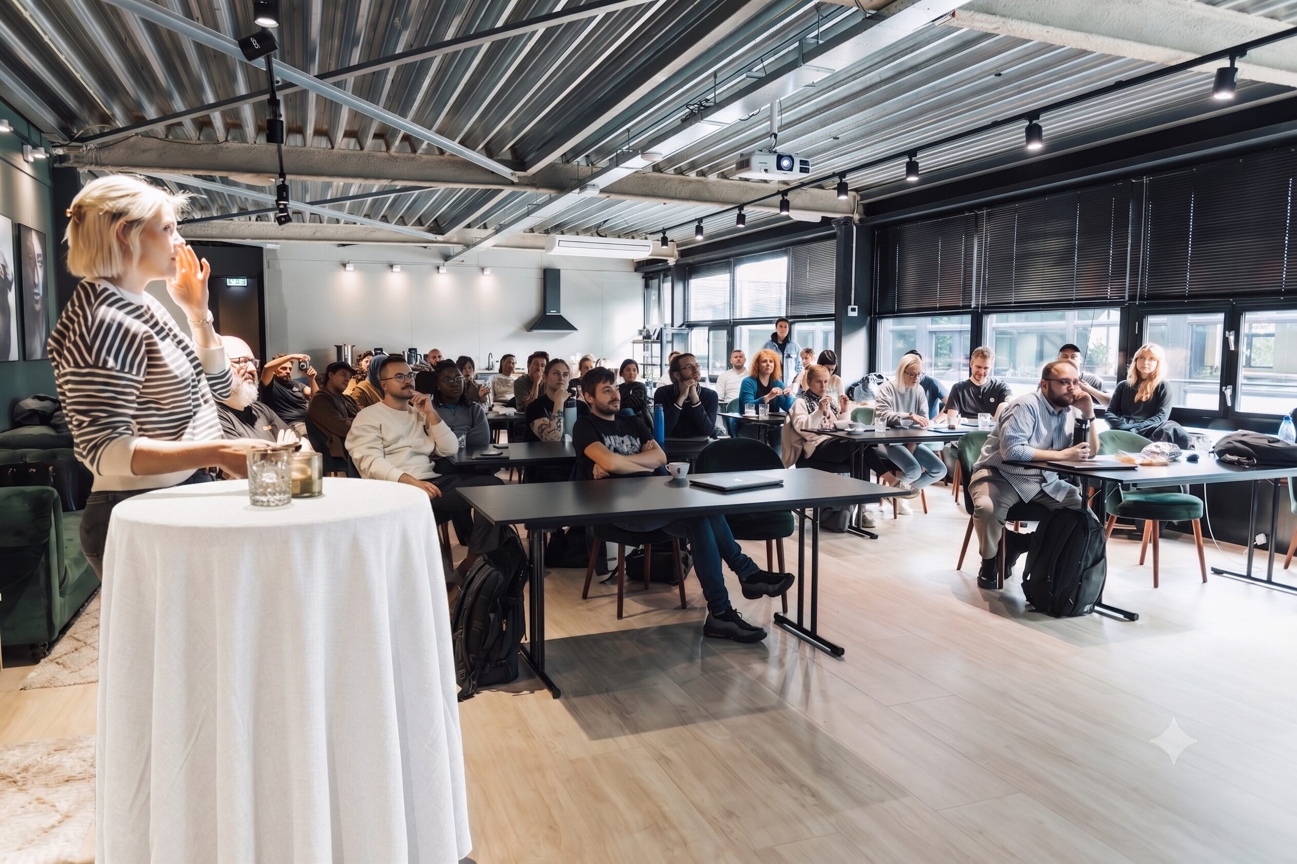 A speaker addressing an attentive audience seated at tables during a presentation, illustrating event content delivery and participant engagement.