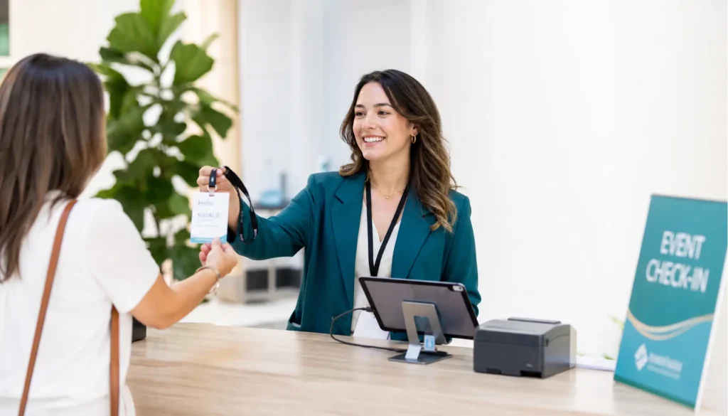 Check-in-Schalter mit iPad, Drucker und Mitarbeiterin, die ein personalisiertes Event-Badge an eine Teilnehmerin ausgibt